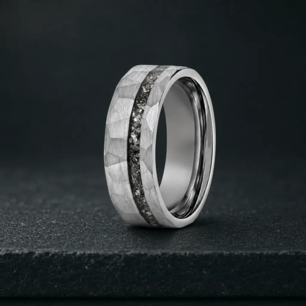 The Vulcan, an 8mm hammered silver tungsten carbide band with a meteorite inlay, standing upright on a dark iron grey stone slab