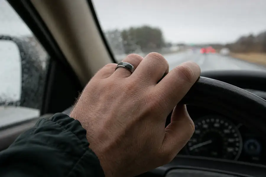 A hand wearing a tungsten band gripping a steering wheel