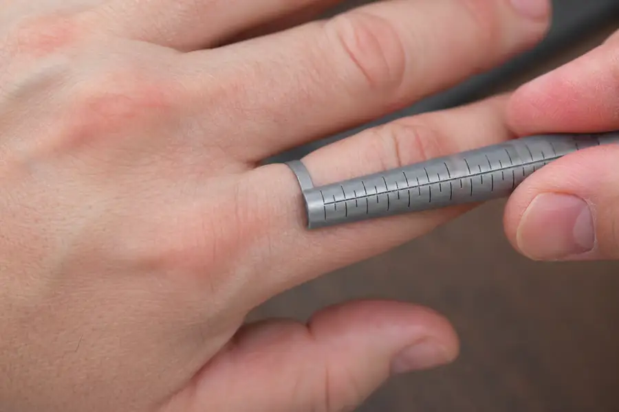 Close view of a hand sliding a graduated metal ring sizer past the knuckle