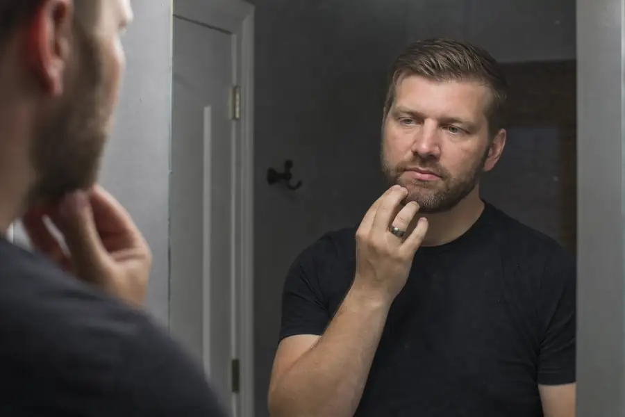 Man trying on a wide tungsten wedding band at a bathroom mirror in the evening