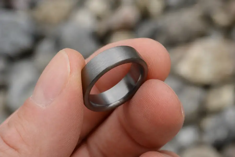 A tungsten band held between fingertips showing its weight and thickness