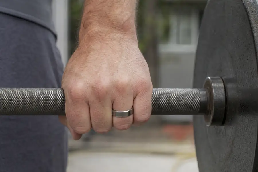 A hand wearing a tungsten band lifting a barbell