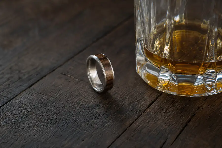 A whiskey barrel inlay ring beside a glass tumbler on dark wood
